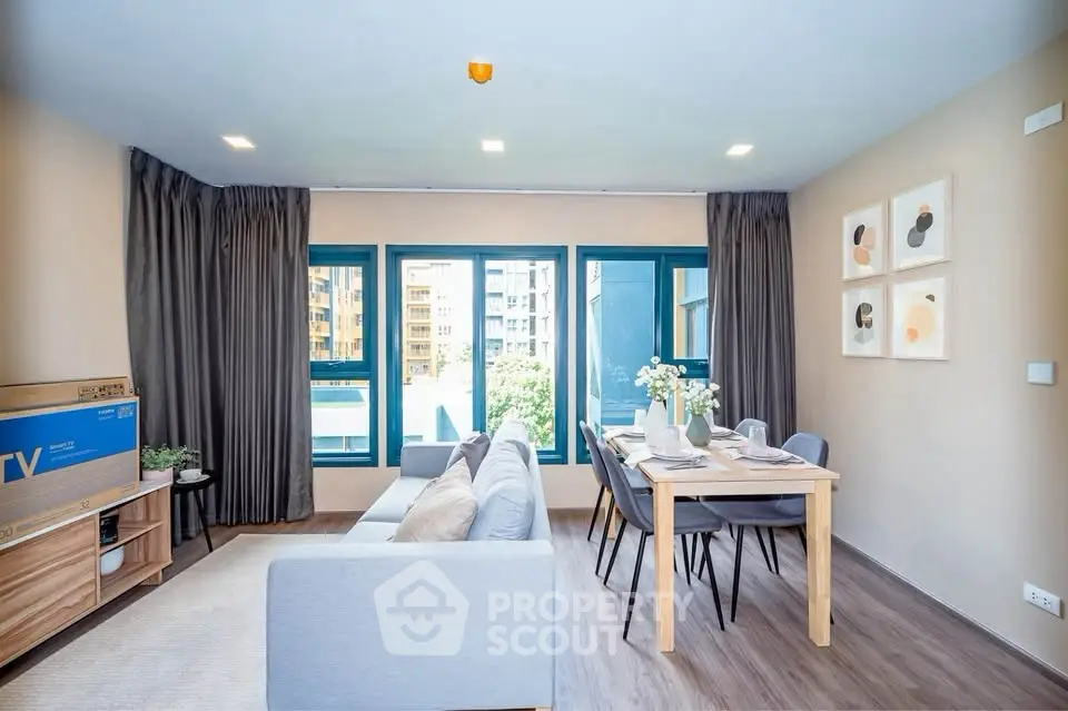 Modern living room with stylish decor and dining area, featuring large windows and natural light.