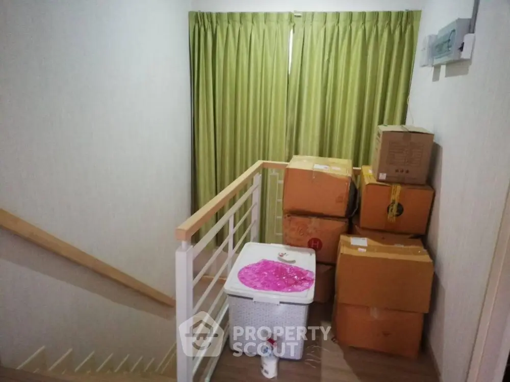 Staircase landing with stacked moving boxes and green curtains.