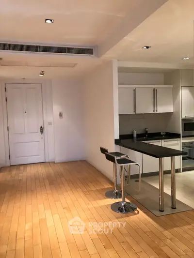 Modern open-layout kitchen with sleek design and wooden flooring, featuring a stylish breakfast bar and stools.
