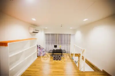 Modern loft space with wooden flooring and minimalist decor, featuring a cozy seating area and built-in shelving.