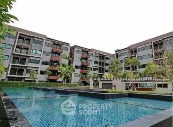 Modern apartment complex with a large swimming pool and lush greenery.