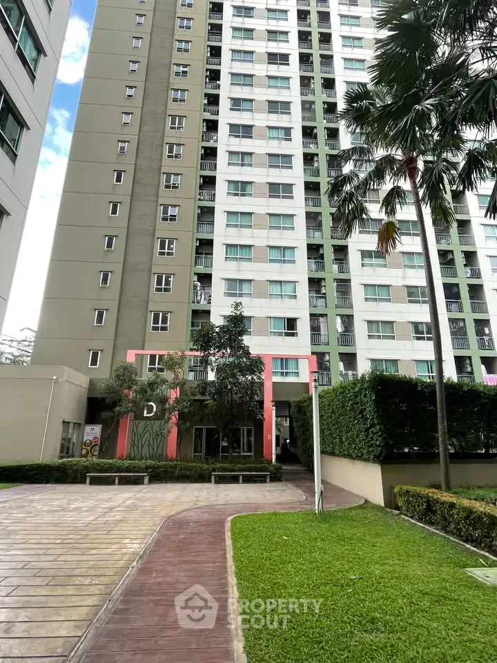 Modern high-rise apartment building with lush green landscaping and clear blue sky.
