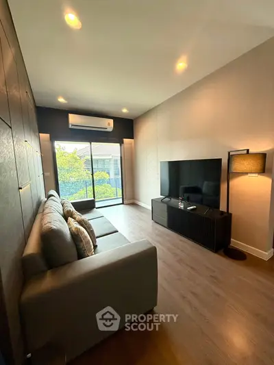 Modern living room with sleek furniture and large TV, featuring a view of the balcony and greenery.