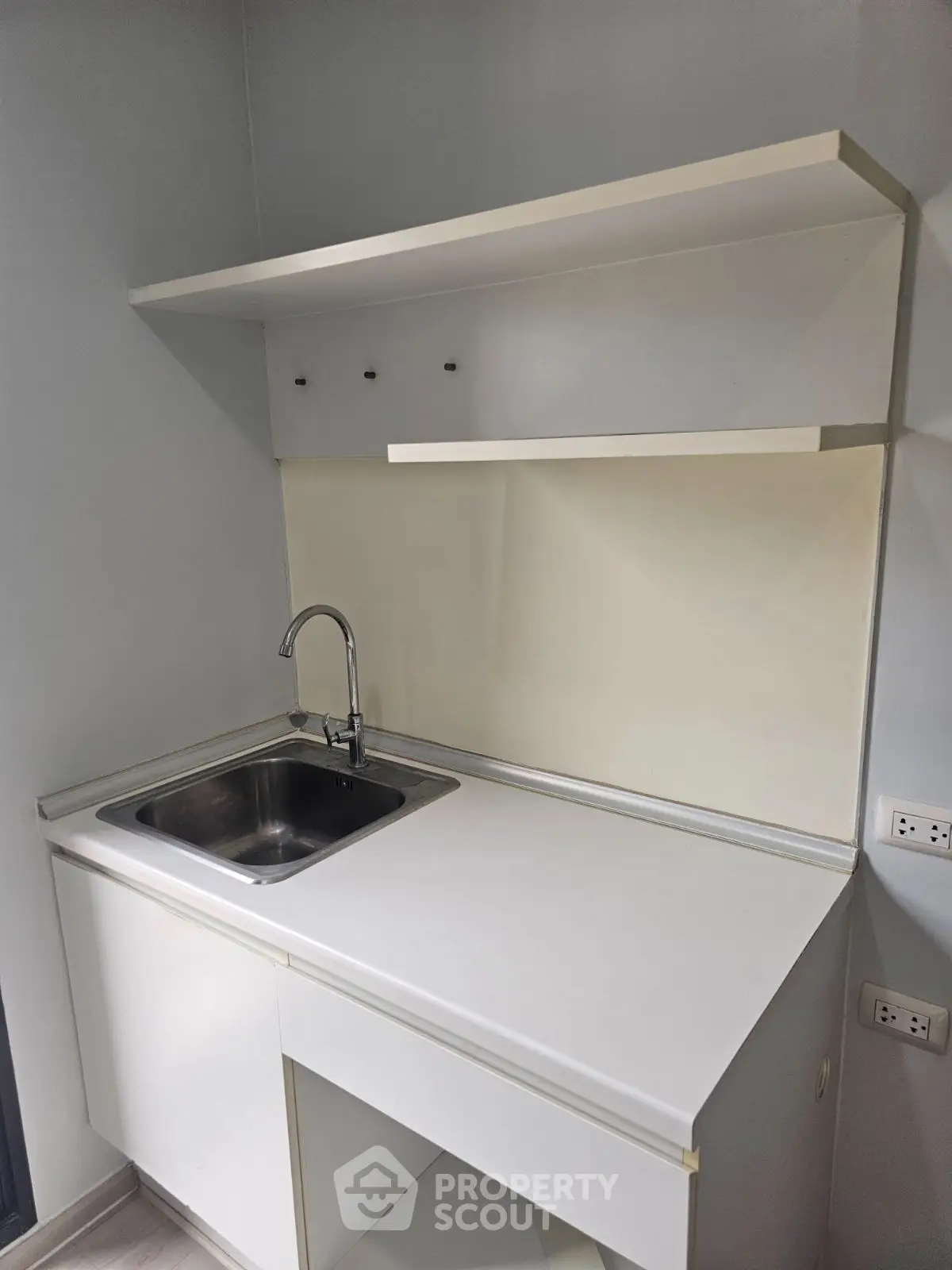 Modern minimalist kitchen with sleek white cabinetry and stainless steel sink, perfect for compact spaces.