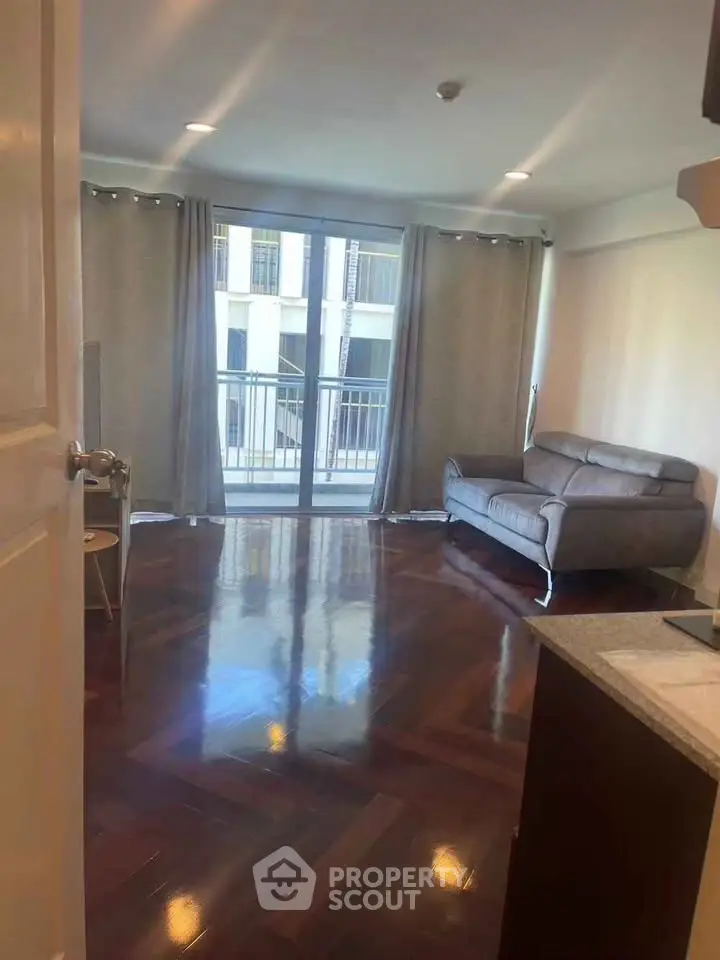 Spacious living room with elegant wooden flooring and modern sofa, featuring a balcony view.