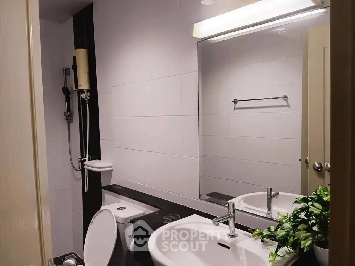 Modern bathroom with sleek fixtures and large mirror, featuring a shower and stylish sink.