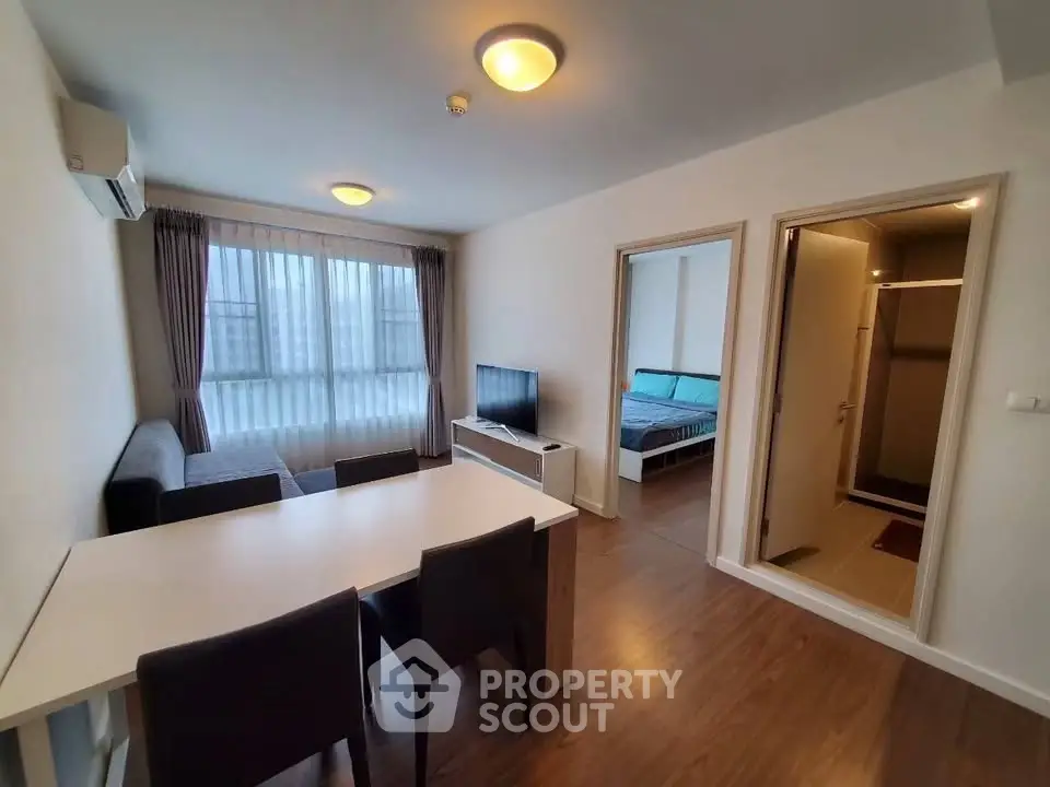 Modern living room with dining area and view into bedroom, featuring sleek furniture and ample natural light.