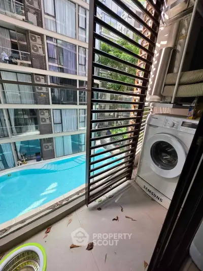 Modern apartment balcony with washing machine overlooking pool and building view.