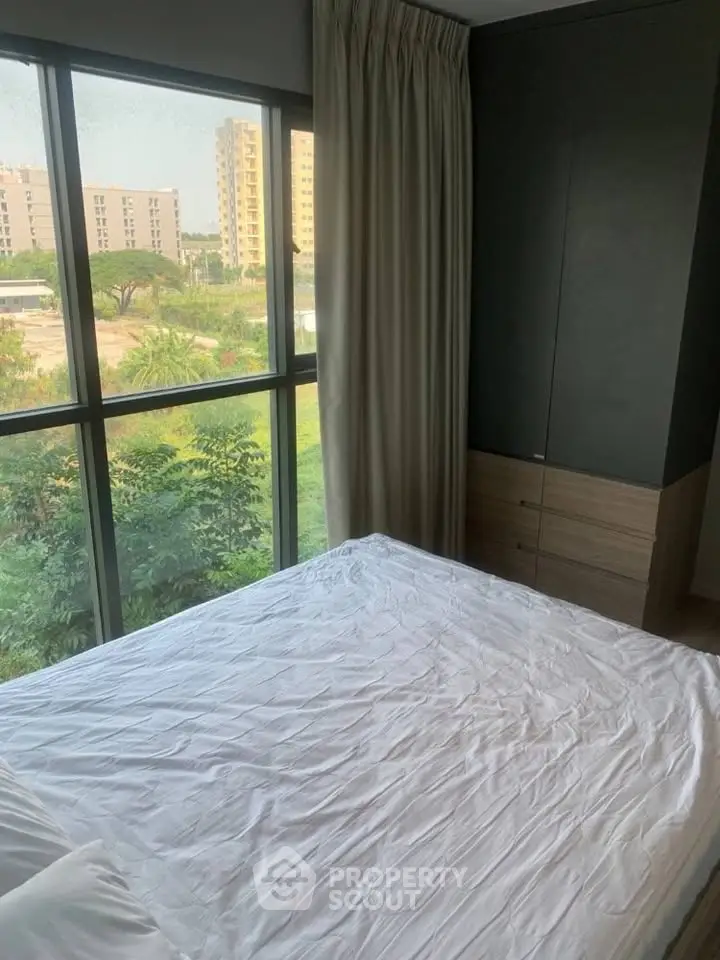 Bright bedroom with large windows offering a lush green view, featuring a cozy bed and modern wardrobe.