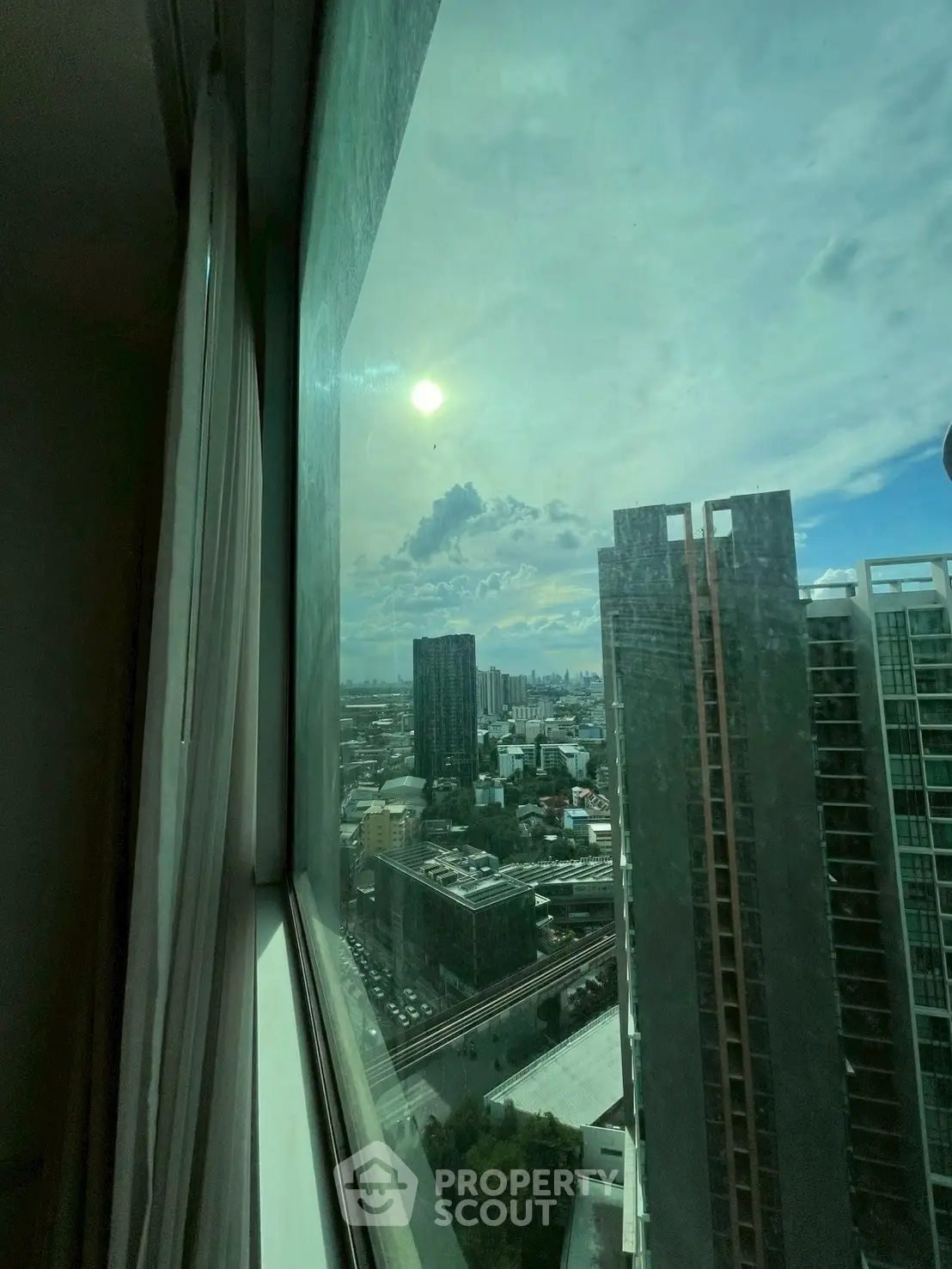 Stunning high-rise city view from a large window, showcasing urban skyline and bright sky.