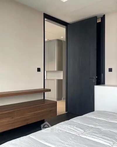 Modern bedroom with sleek wooden furniture and open door to kitchen area.