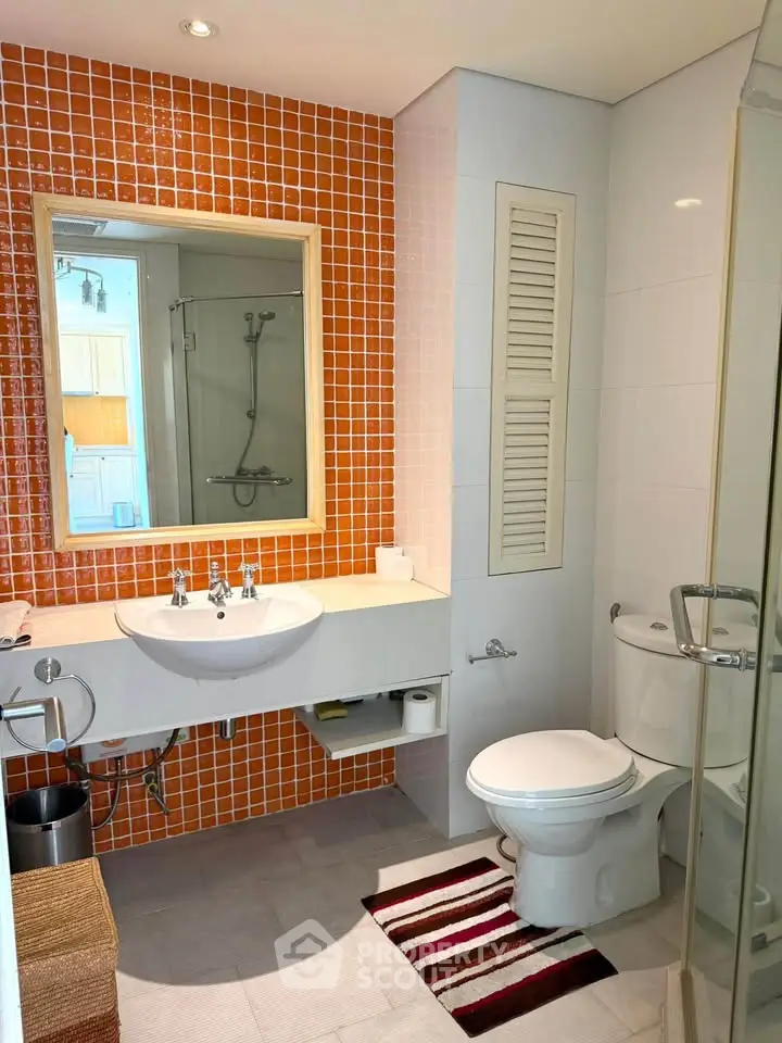 Modern bathroom with orange tiled wall, glass shower, and sleek fixtures.