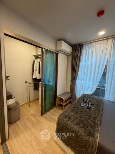 Cozy bedroom with walk-in closet and modern decor, featuring large window with sheer curtains.