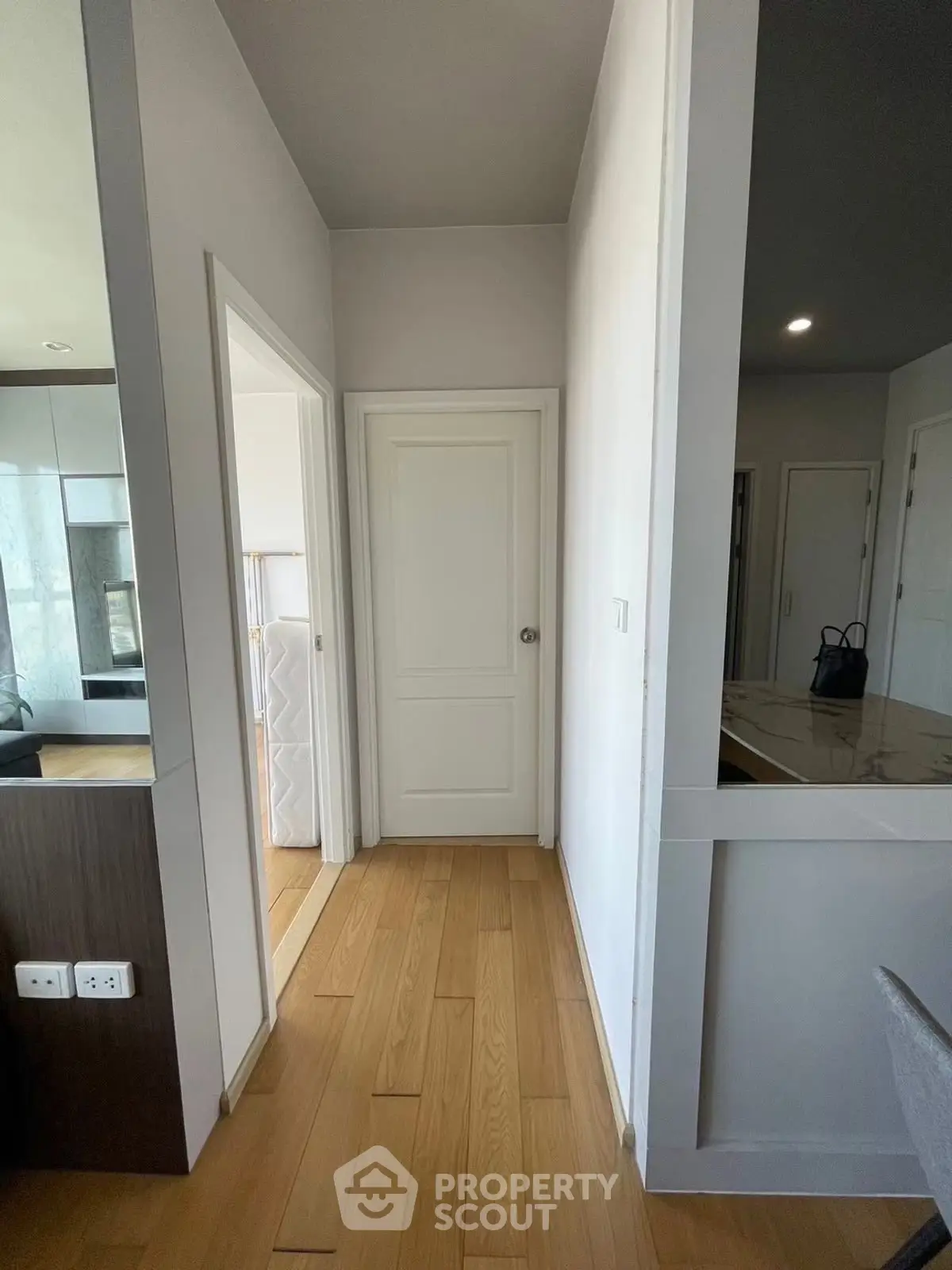 Modern apartment hallway with wooden flooring and white doors, showcasing sleek interior design.