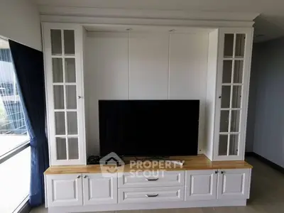 Spacious living room with custom-built white entertainment center and large flat-screen TV, ample storage, and natural light.