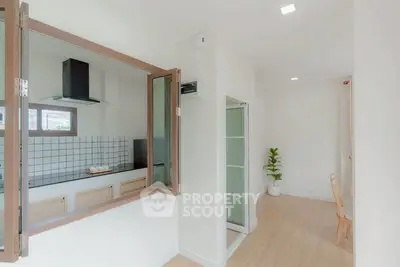 Modern kitchen with open layout and sleek design, featuring a window pass-through and light wood flooring.