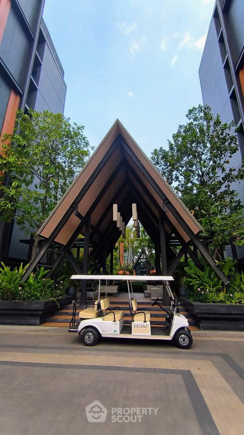 Modern building entrance with unique architecture and golf cart, surrounded by lush greenery.