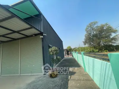 Modern industrial building exterior with spacious driveway and vibrant green fence.