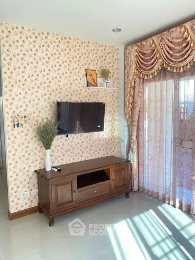 Charming living room with floral wallpaper and elegant curtains, featuring a mounted TV and wooden cabinet.