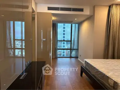 Spacious bedroom with large window offering city view and elegant wooden flooring.
