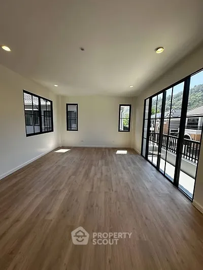 Spacious living room with large windows and wooden flooring, offering ample natural light and a serene view.