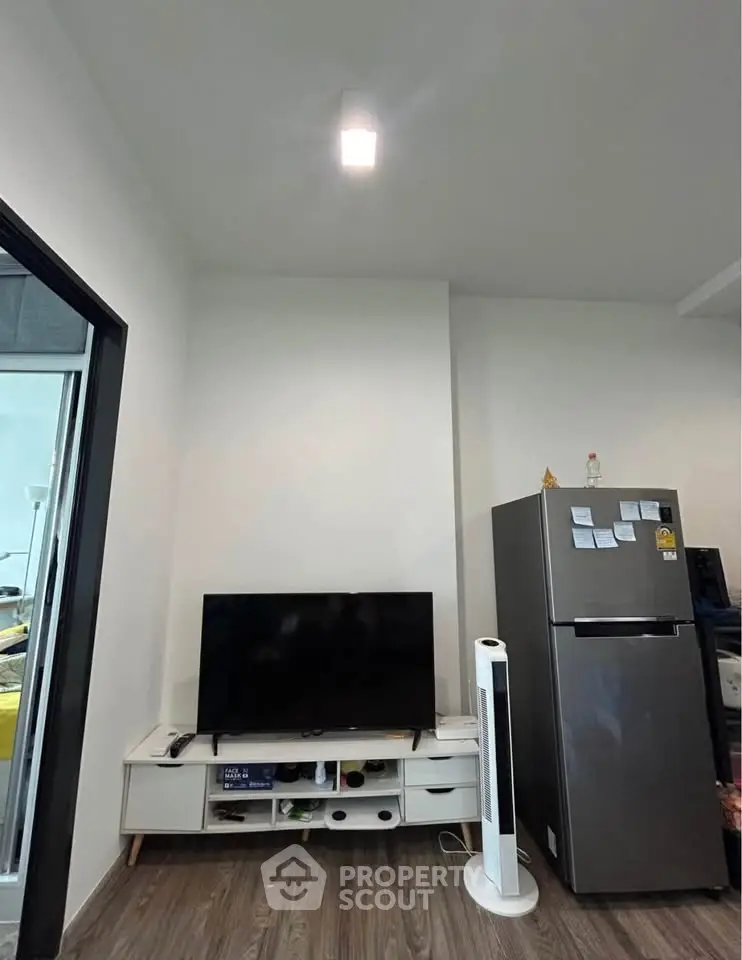 Modern living room with sleek TV setup and stainless steel fridge, perfect for urban living.