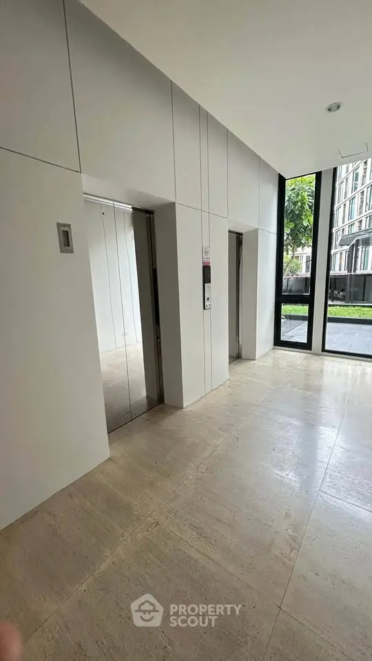 Modern building lobby with elevators and large windows offering garden view.