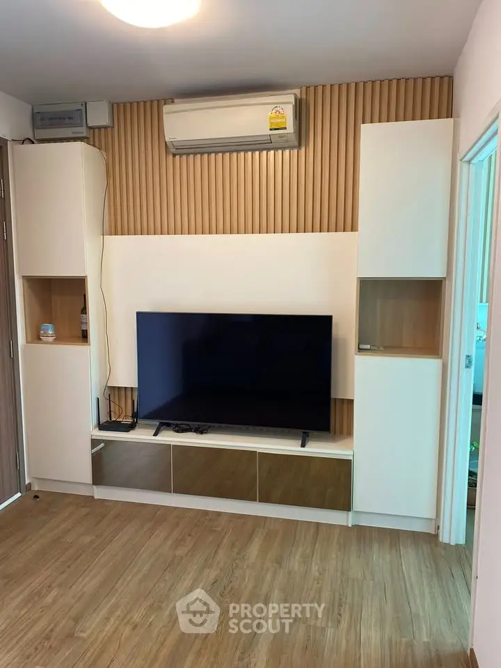 Modern living room with sleek TV unit and wooden flooring, featuring built-in storage and air conditioning.