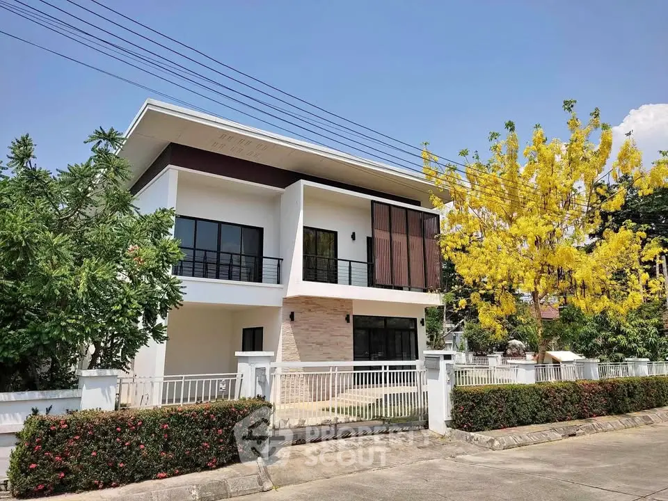 Modern two-story house with large windows and lush garden in a serene neighborhood.