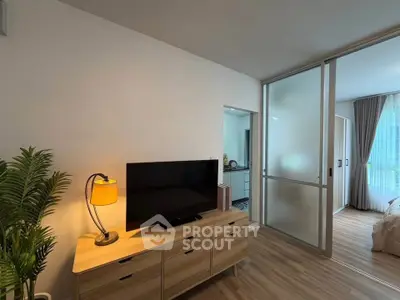 Modern living room with TV, wooden furniture, and sliding glass doors leading to a bright bedroom.
