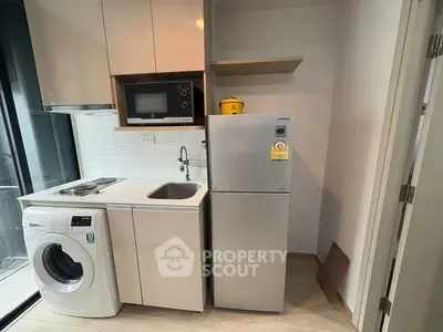 Compact kitchen with modern appliances including fridge, microwave, and washing machine in cozy apartment.