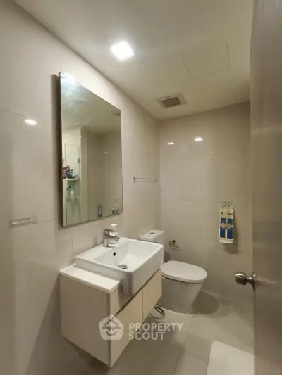 Modern bathroom with sleek fixtures and minimalist design, featuring a wall-mounted sink and large mirror.