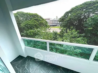 Spacious balcony with safety netting and lush green view, perfect for relaxation.