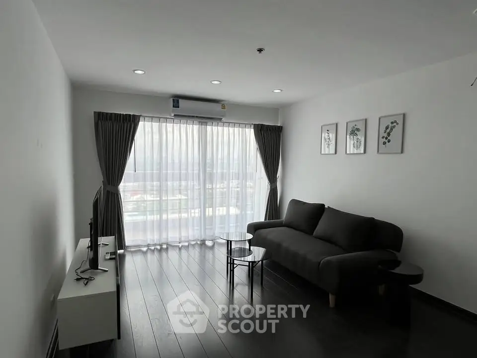 Modern living room with sleek black sofa, stylish decor, and large window offering natural light.