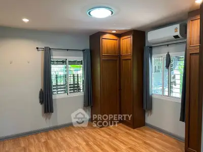 Spacious bedroom with wooden flooring and built-in wardrobes, featuring air conditioning and ample natural light.