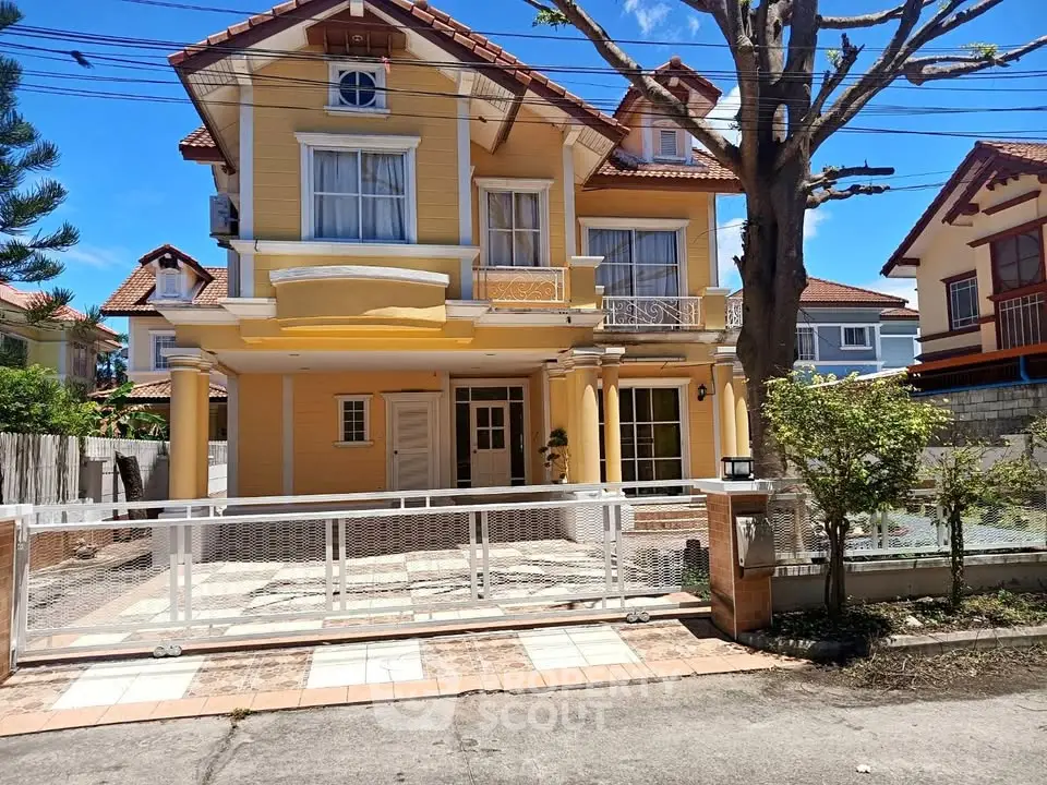 Charming two-story yellow house with gated driveway and lush greenery.