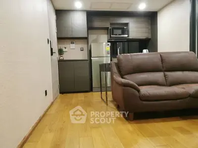 Modern living room with sleek kitchen, featuring wooden flooring and contemporary furniture.