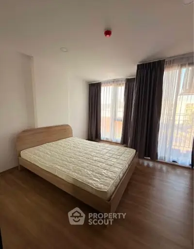 Spacious bedroom with large windows and wooden flooring in modern apartment.