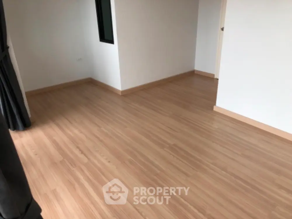 Spacious empty room with wooden flooring and natural light.