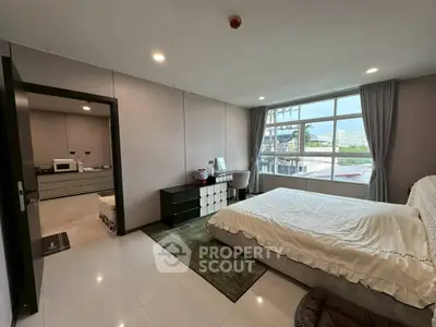Spacious bedroom with large window offering city views, modern furnishings, and ample natural light.