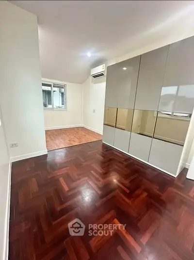 Spacious room with elegant wooden flooring and modern cabinetry, perfect for versatile living.