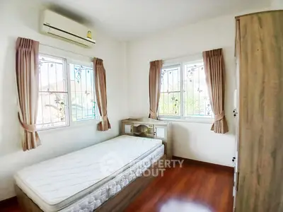 Cozy bedroom with natural light and wooden flooring, featuring a single bed and air conditioning.