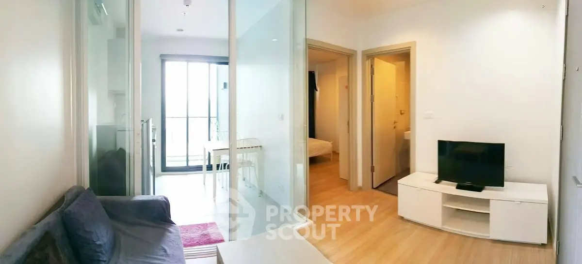 Modern living room with glass doors leading to a bright dining area and bedroom, featuring sleek furniture.