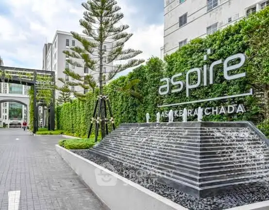 Modern condominium entrance with lush greenery and stylish water feature.