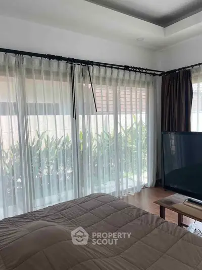 Cozy bedroom with large windows and garden view, featuring modern decor and natural light.