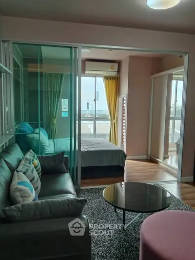 Modern condo interior with cozy living room and bedroom, featuring glass partition and city view.