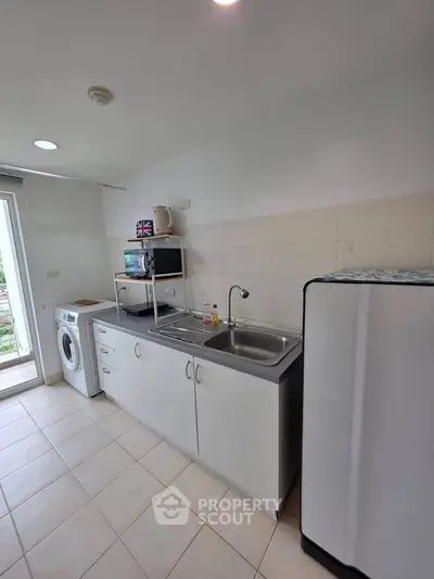 Modern kitchen with washing machine and fridge in a compact layout, ideal for efficient living.