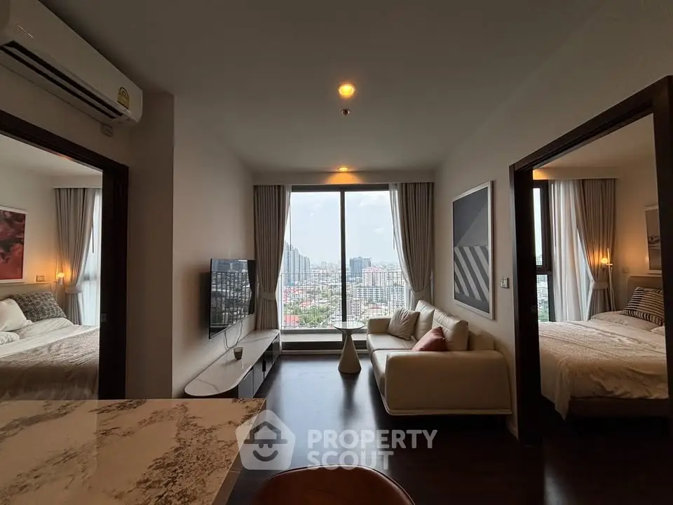 Modern apartment living room with city view, featuring stylish decor and two adjacent bedrooms.