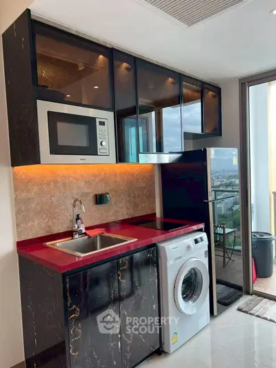 Modern kitchen with sleek black cabinets, red countertop, and city view balcony access.