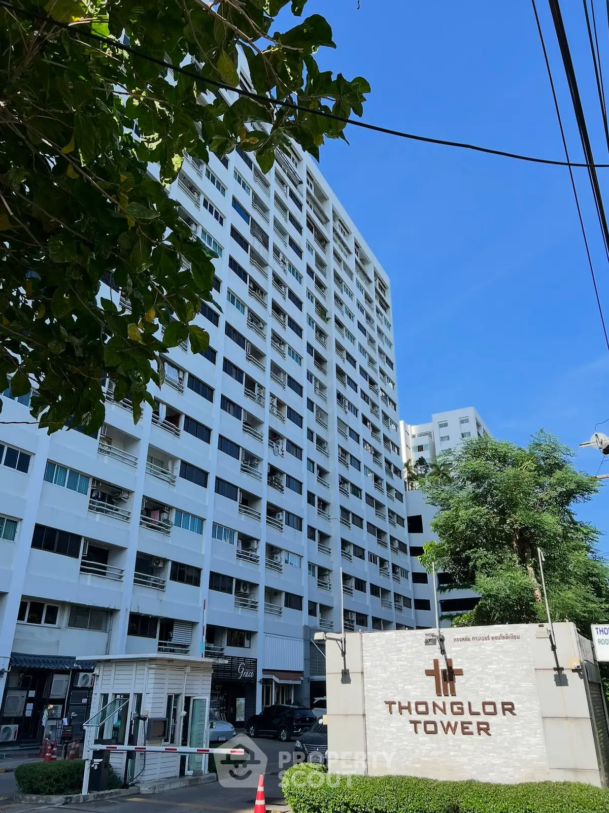 Modern high-rise building exterior of Thonglor Tower with lush greenery and clear blue sky.